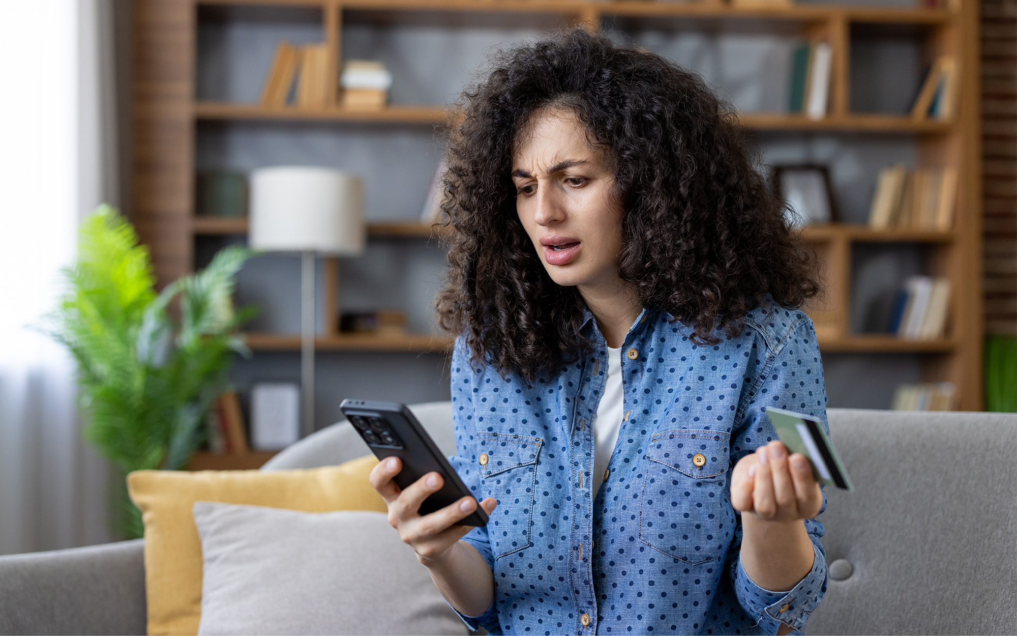 Customer looking at phone with puzzled face holding credit card in the other hand